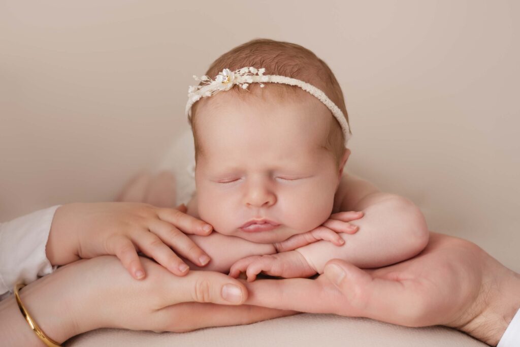 Baby girl asleep with her head on her hands resting in her parents hands with her little brothers hand providing support
