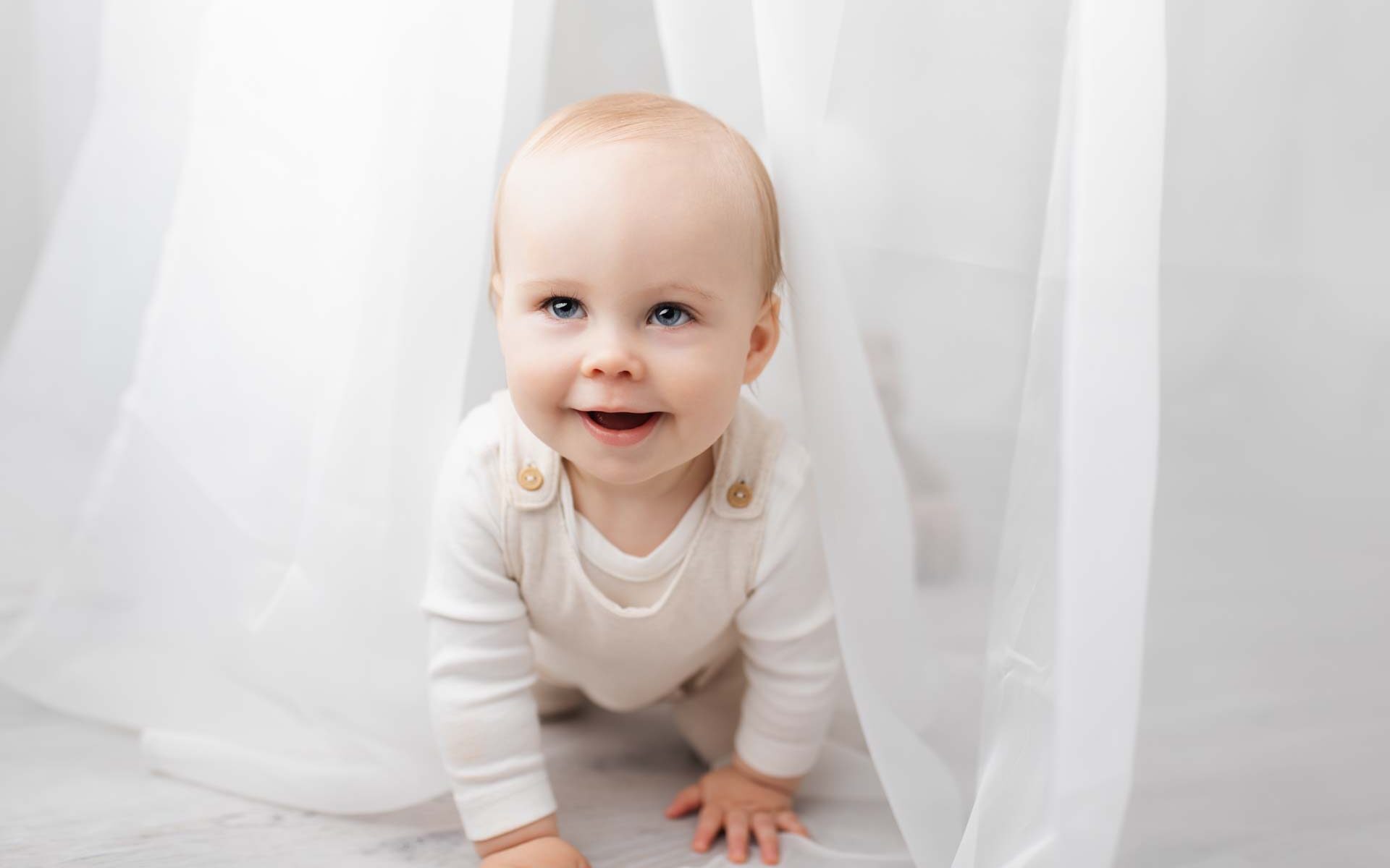 First birthday boy plays peekaboo with the photographer through a net curtain