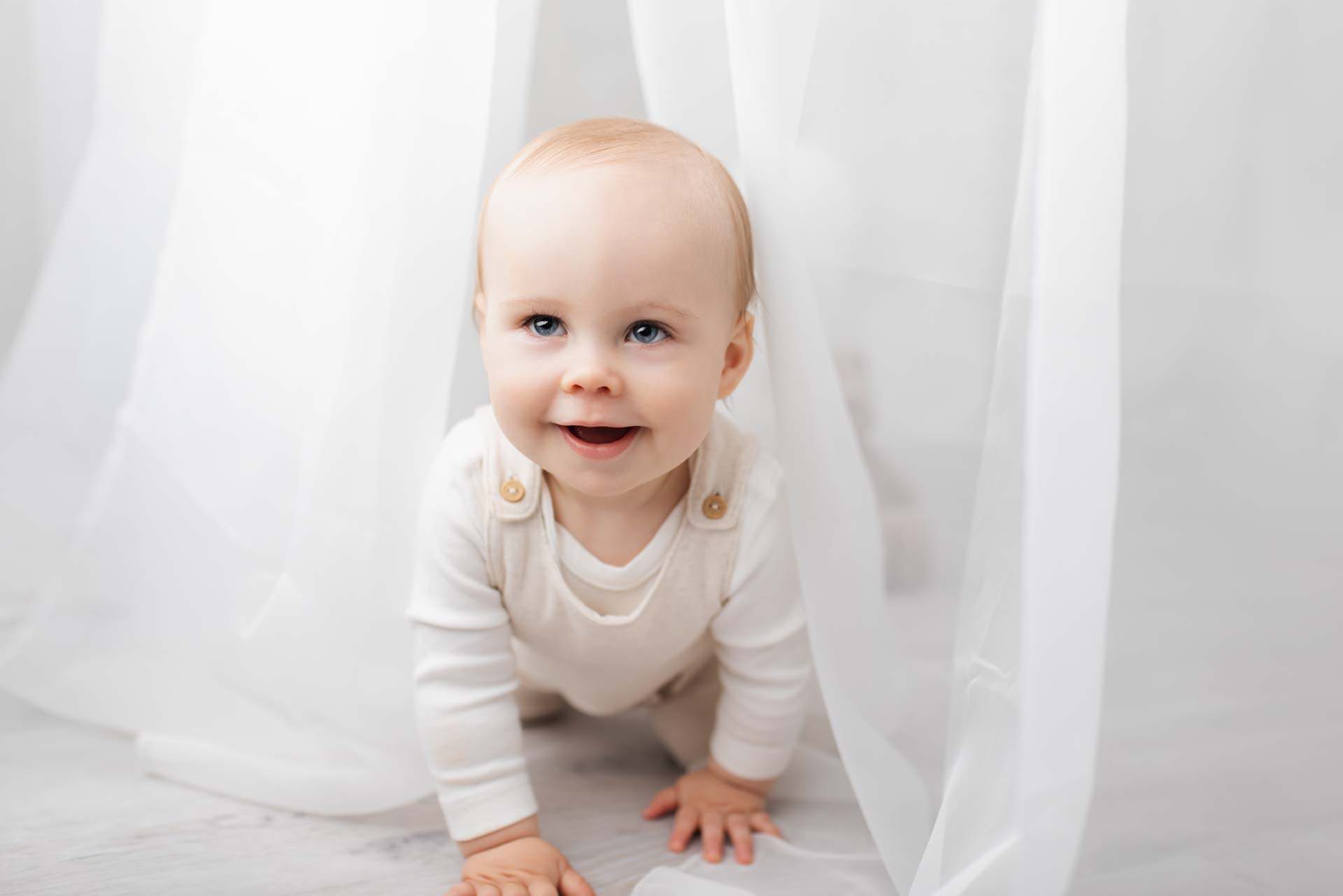 First birthday boy plays peekaboo with the photographer through a net curtain