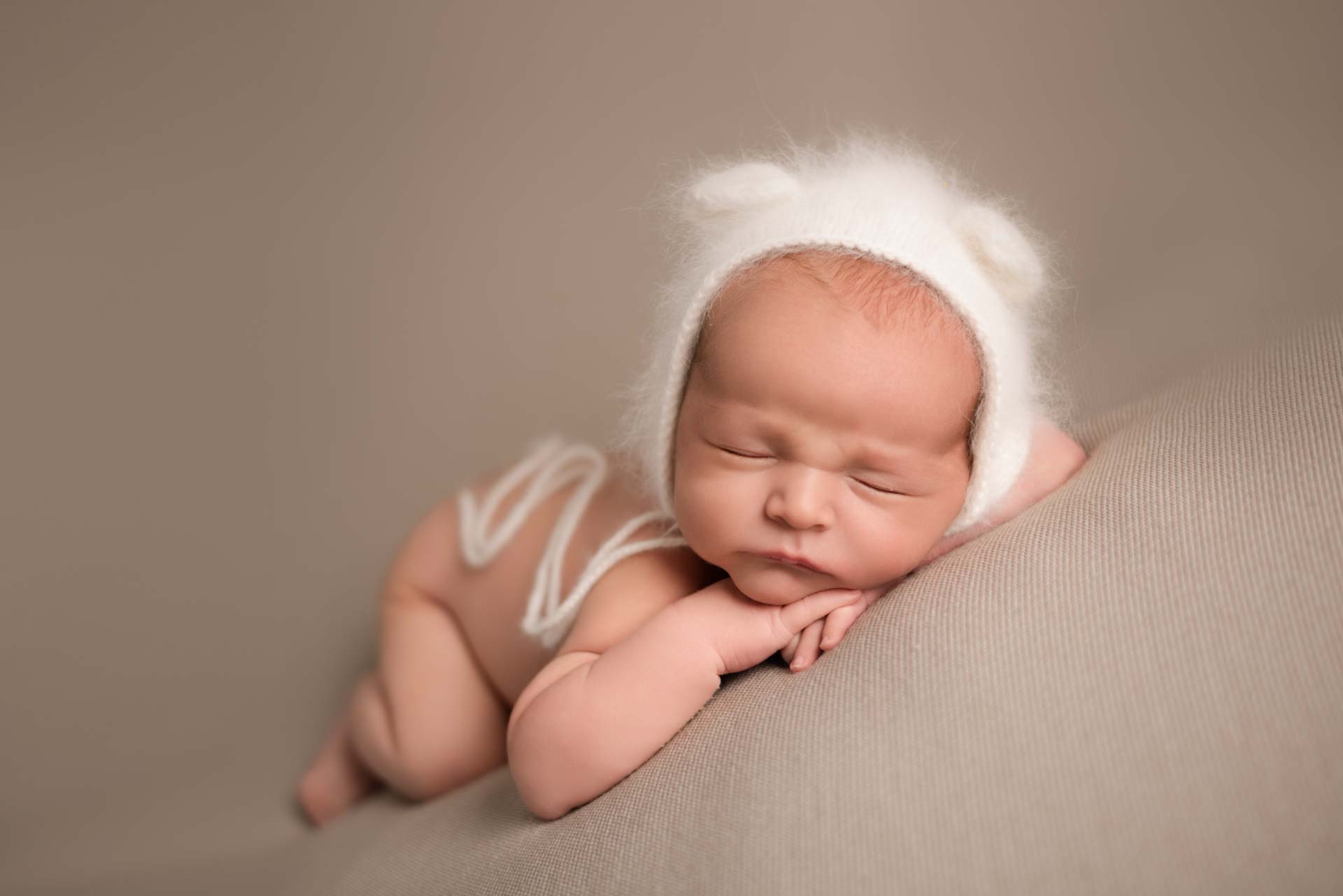 Newborn baby wearing a wooly bonnet with bear ears and long tassels