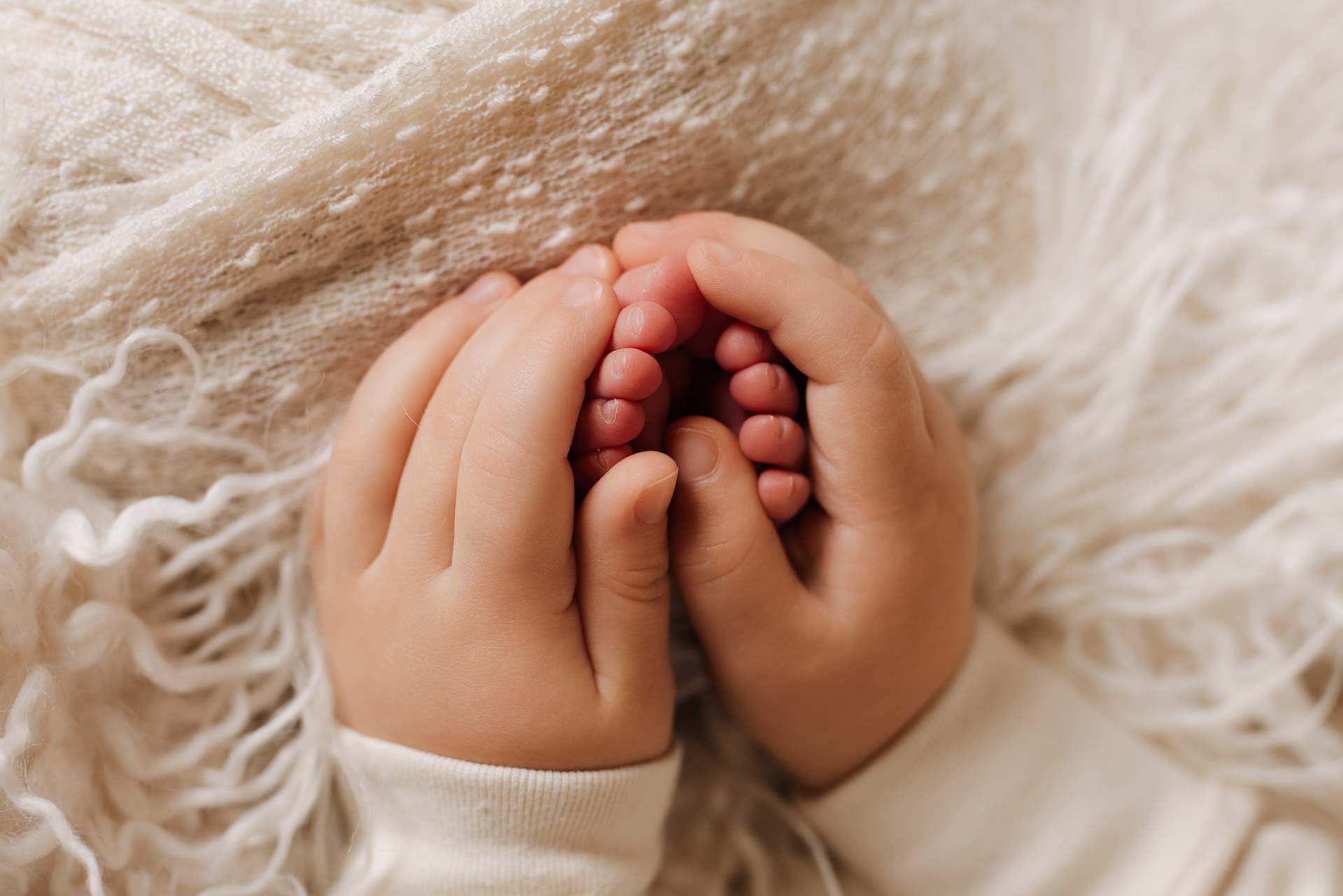 Photograph of a baby boy's little hands holding is new sisters toes