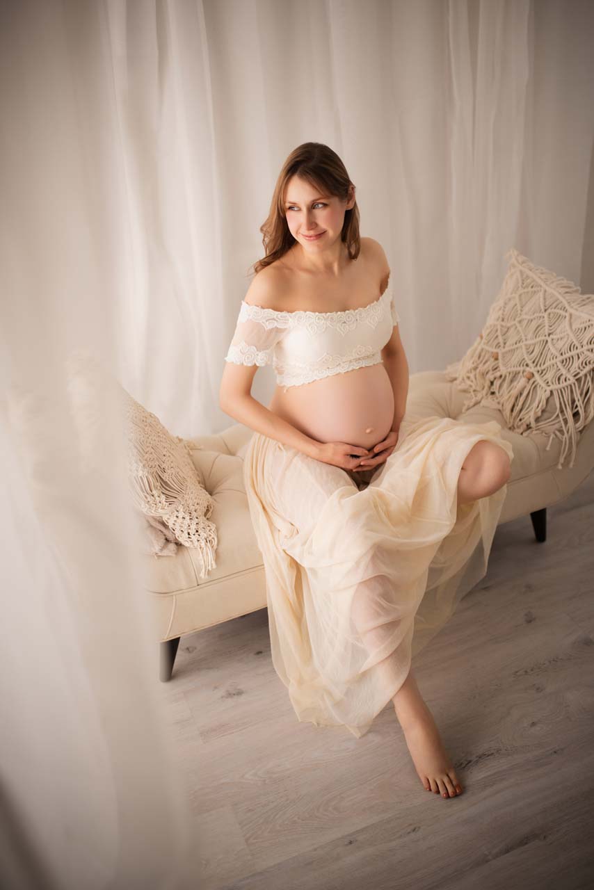 Expectant mother sitting on a chaise in the photographer's studio dreaming about her baby.