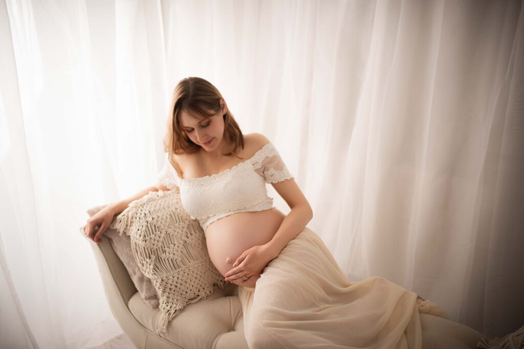 Pregnant lady lying on a chaise holding her bump during her maternity photoshoot