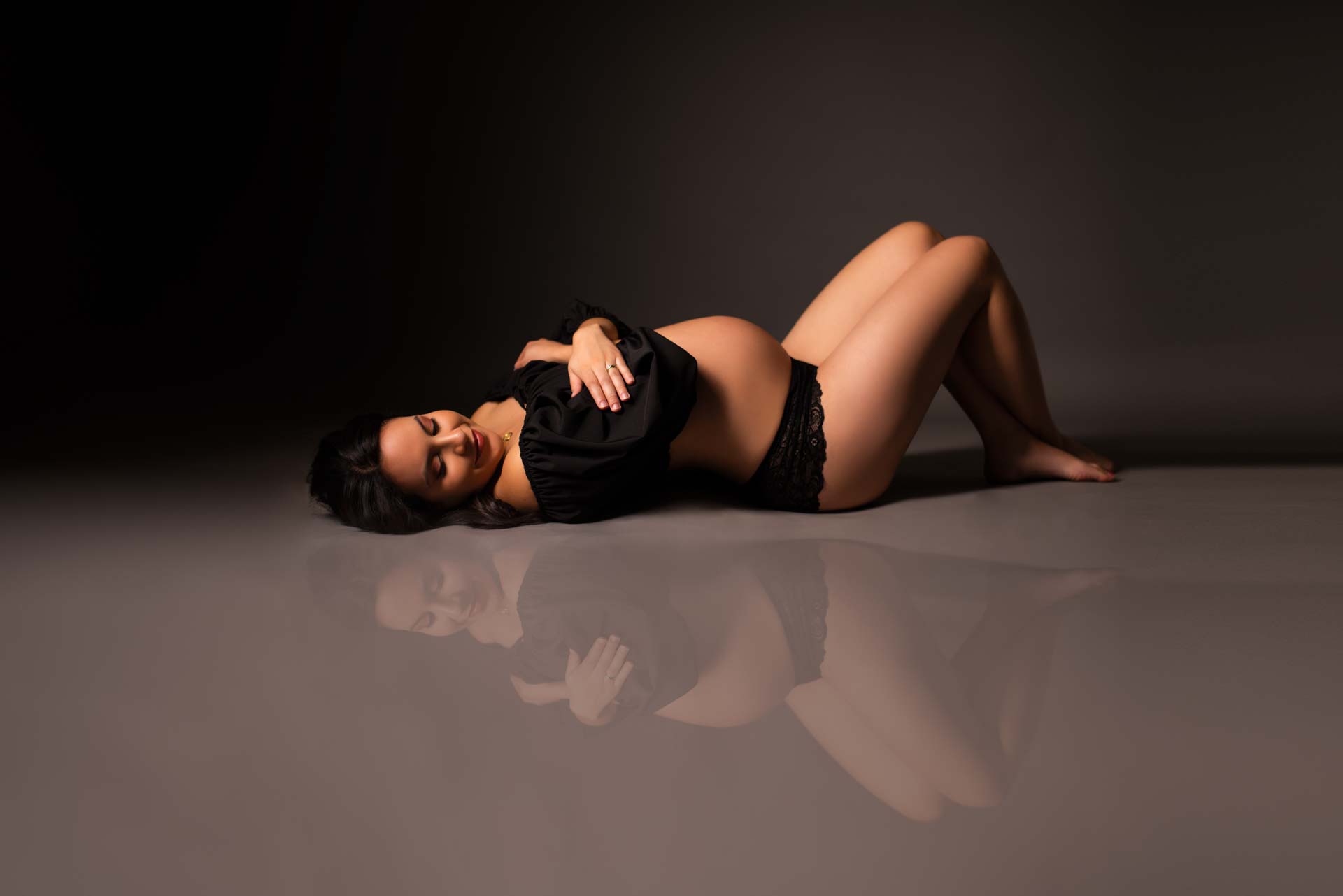 Pregnant women lying on the floor wearing black. You can see her reflection on the floor