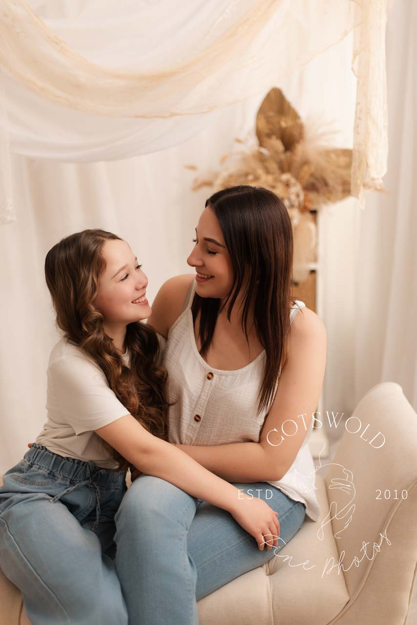 Mummy playing with her son. They are sitting on a chaise and she is tickling him