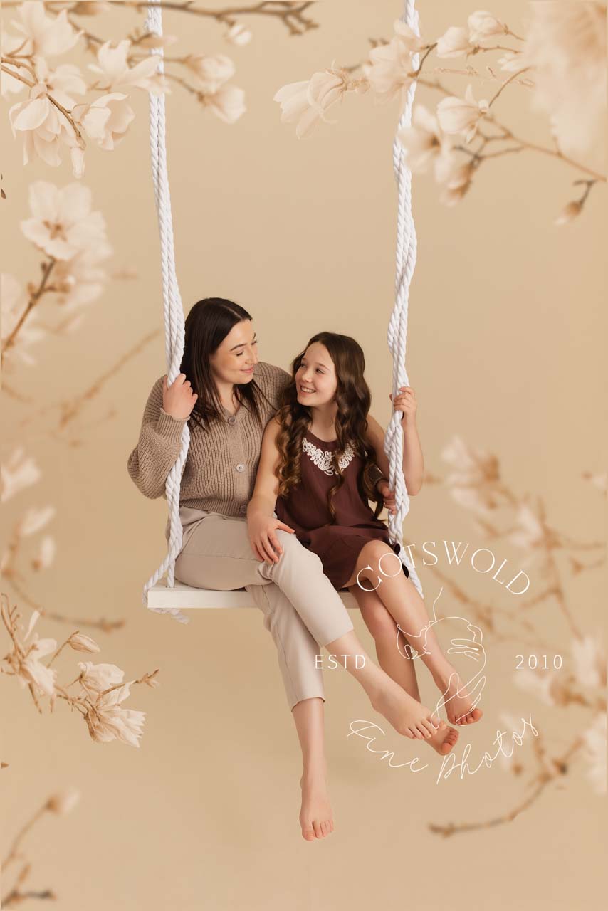 Mother and daughter sitting on a swing surrounded by blossom for their mothers day photos