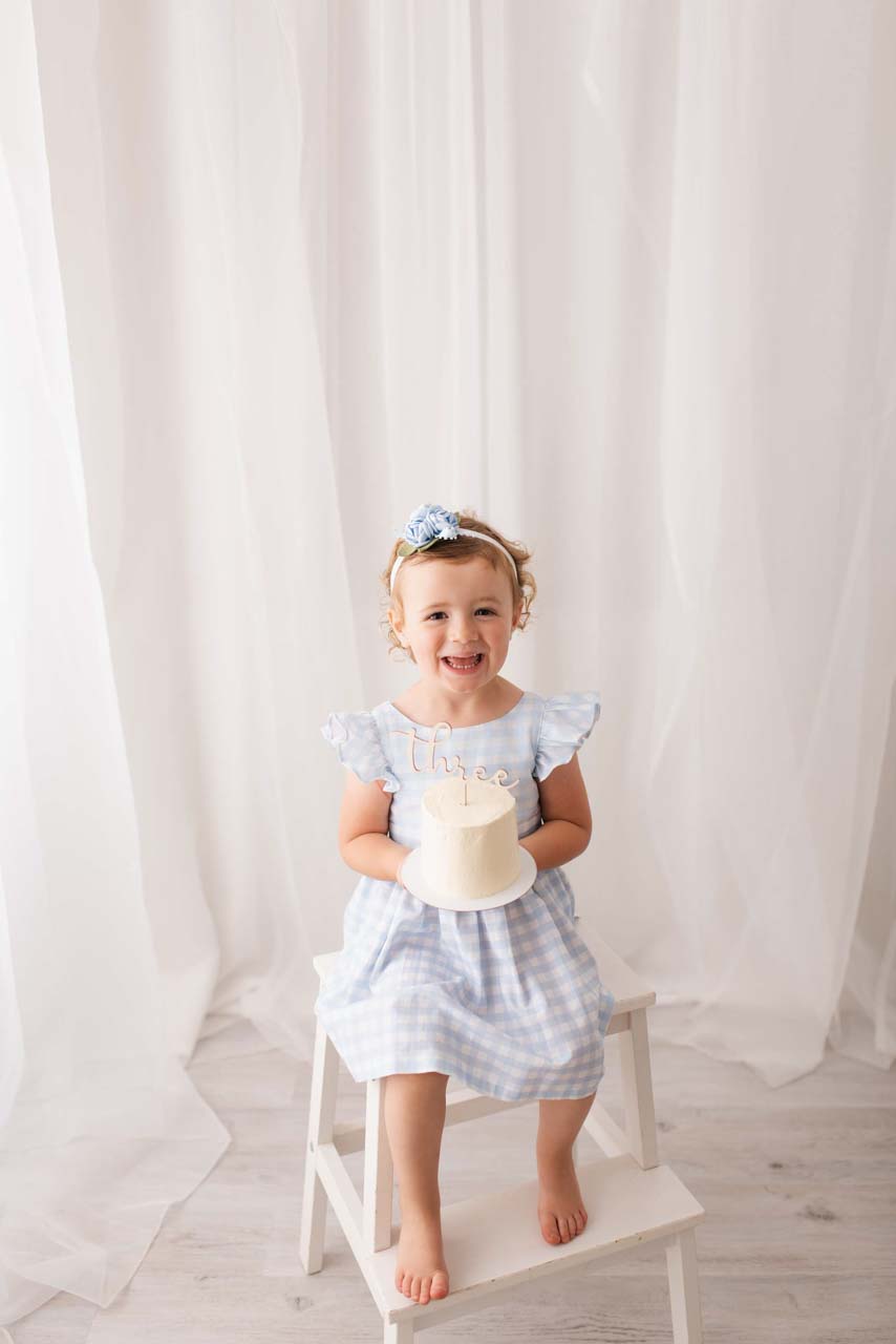 Smiling three year old holds her birthday cake in her hands