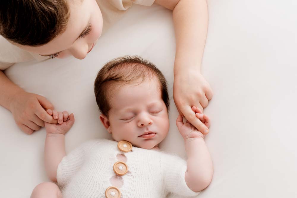 4 year old boy holds the hands of his sleeping baby brother