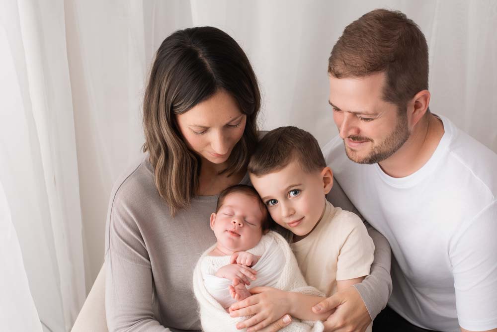 Family of four sit cuddling their new arrival in the photography studio
