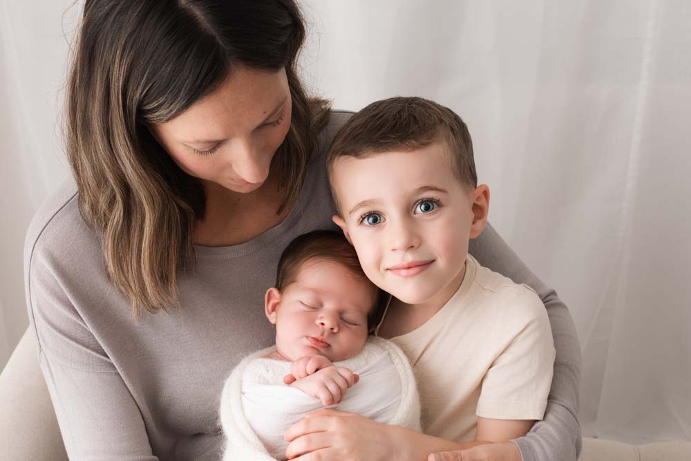 Mother and son sit cuddling their new baby