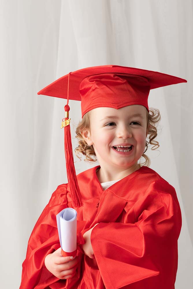 Child wearing a red graduation gown and mortarboard for her nursery photos