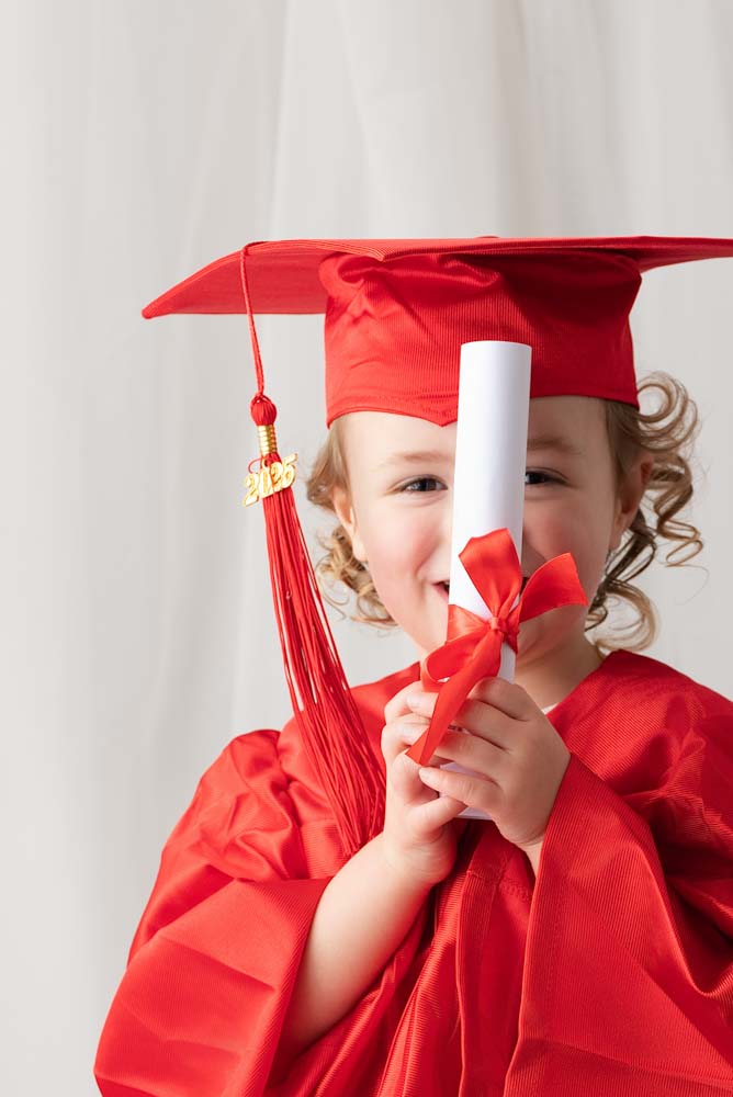 Graduation style photo for a nursery photoshoot. The model is dressed all in red and is holding her diploma in front of her face