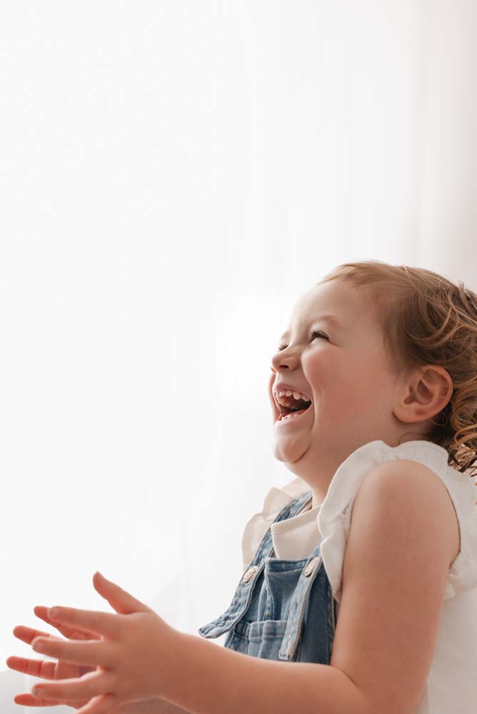 Three year old girl laughs and claps during her preschool photoshoot