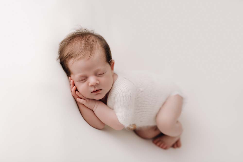Baby boy asleep on his side posed with his hands under his head