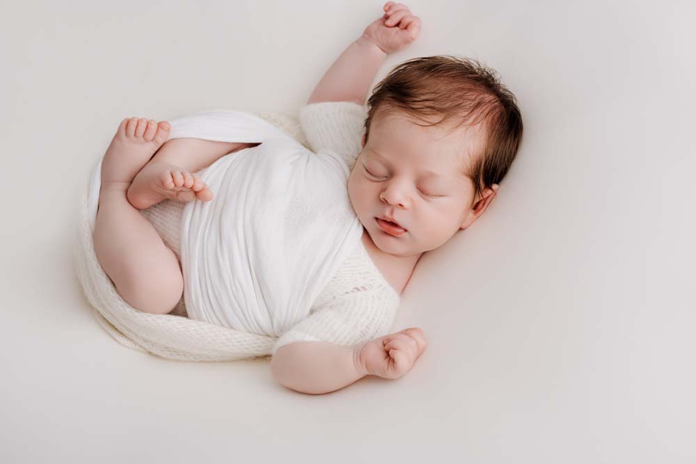Sleeping baby boy lying on the photographers beanbag with his arms over his head