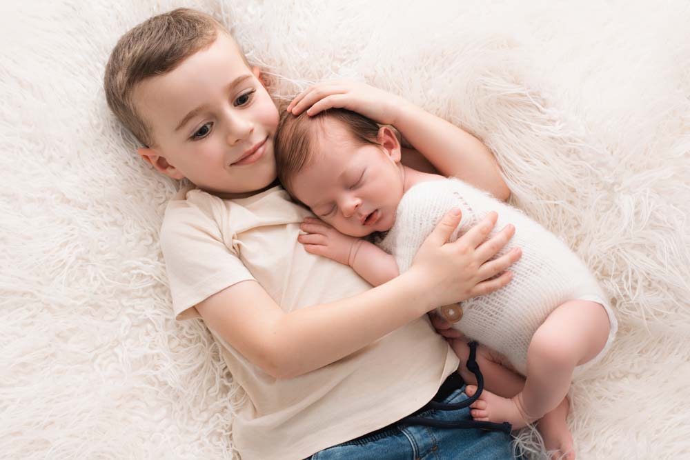 Big brother lying on a fluffy blanket cuddling his new baby brother