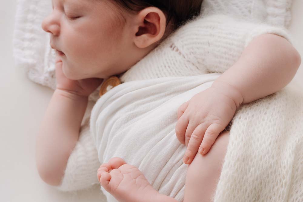 Newborn baby dressed in white holding his knee