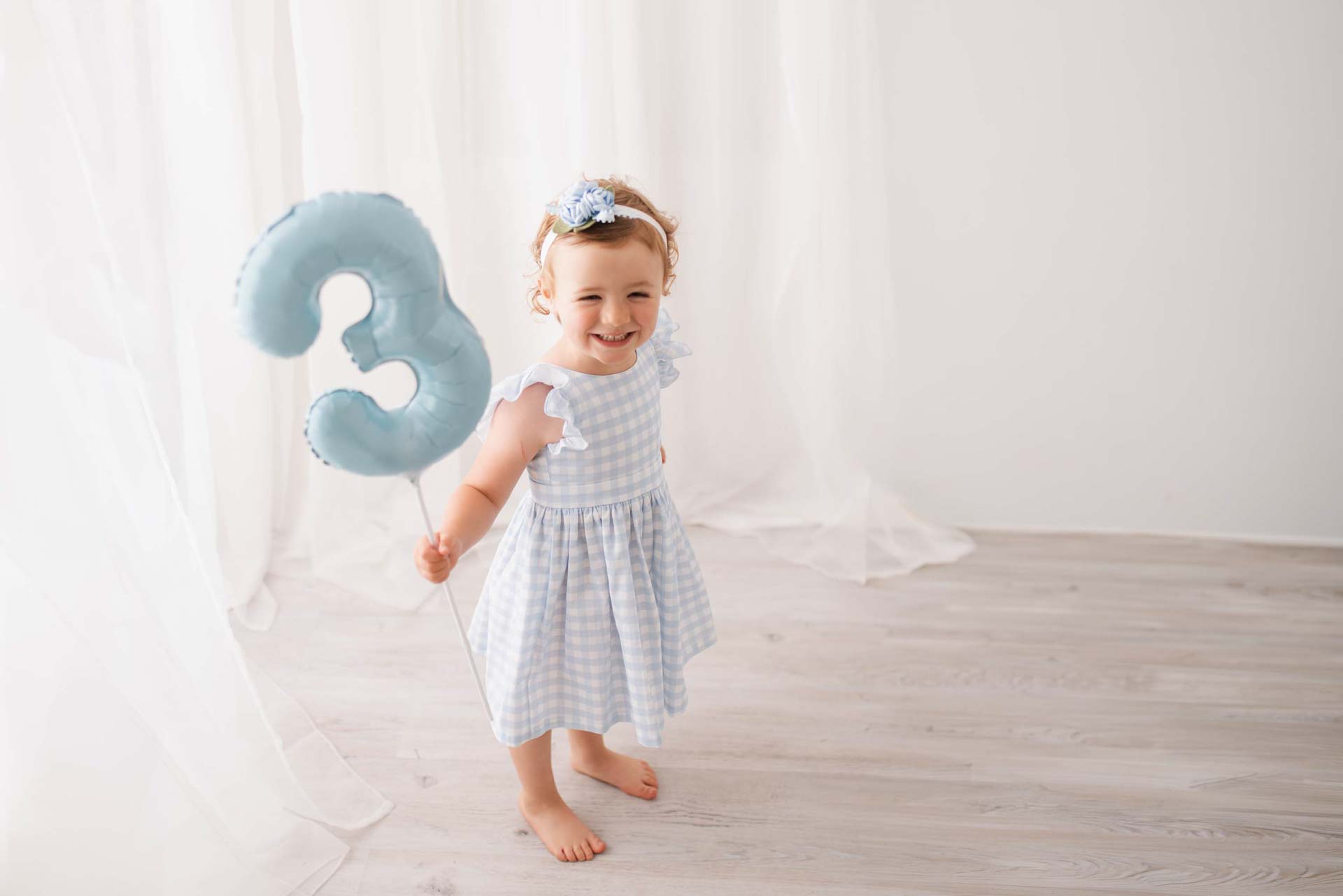 Girl holding a blue number 3 balloon with a big smile on her face
