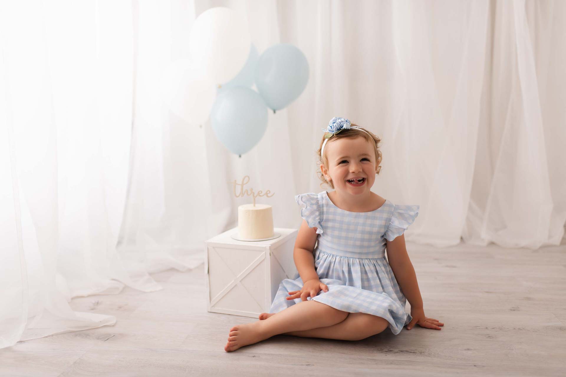 Girl celebrating her third birthday sits next to a white cake with her tongue out