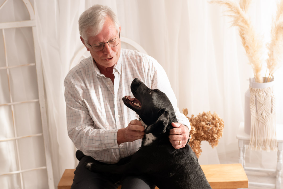 Grandfather plays with the family black labrador whilst the rest of the family wait for their photos