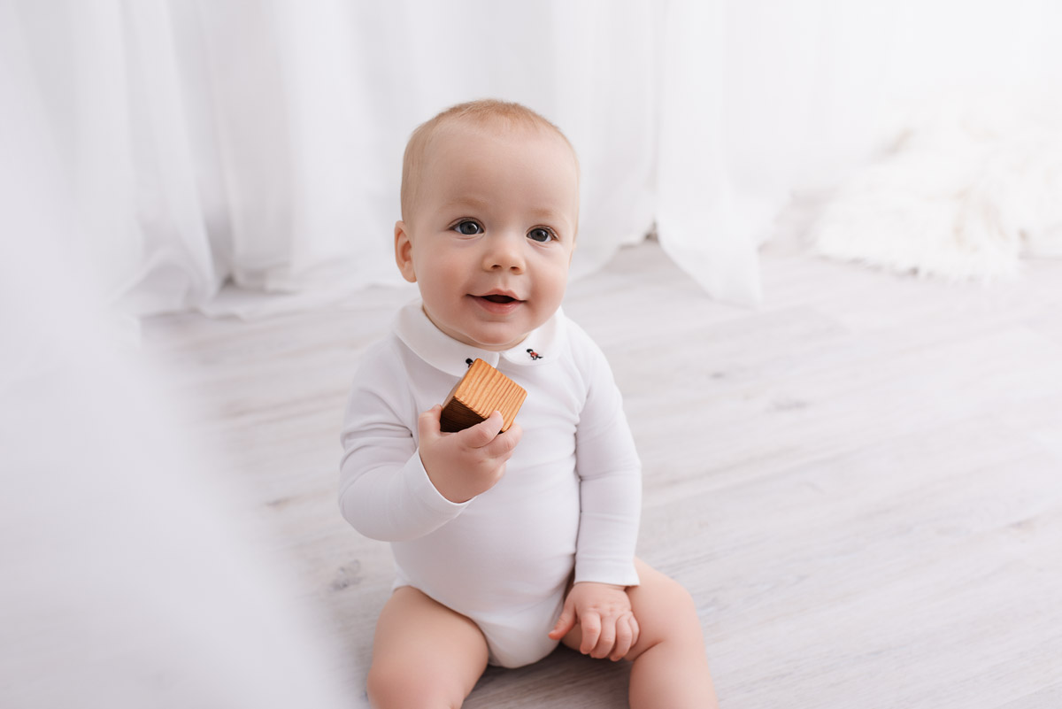 Smiling baby boy holds a wooden block and looks at the camera