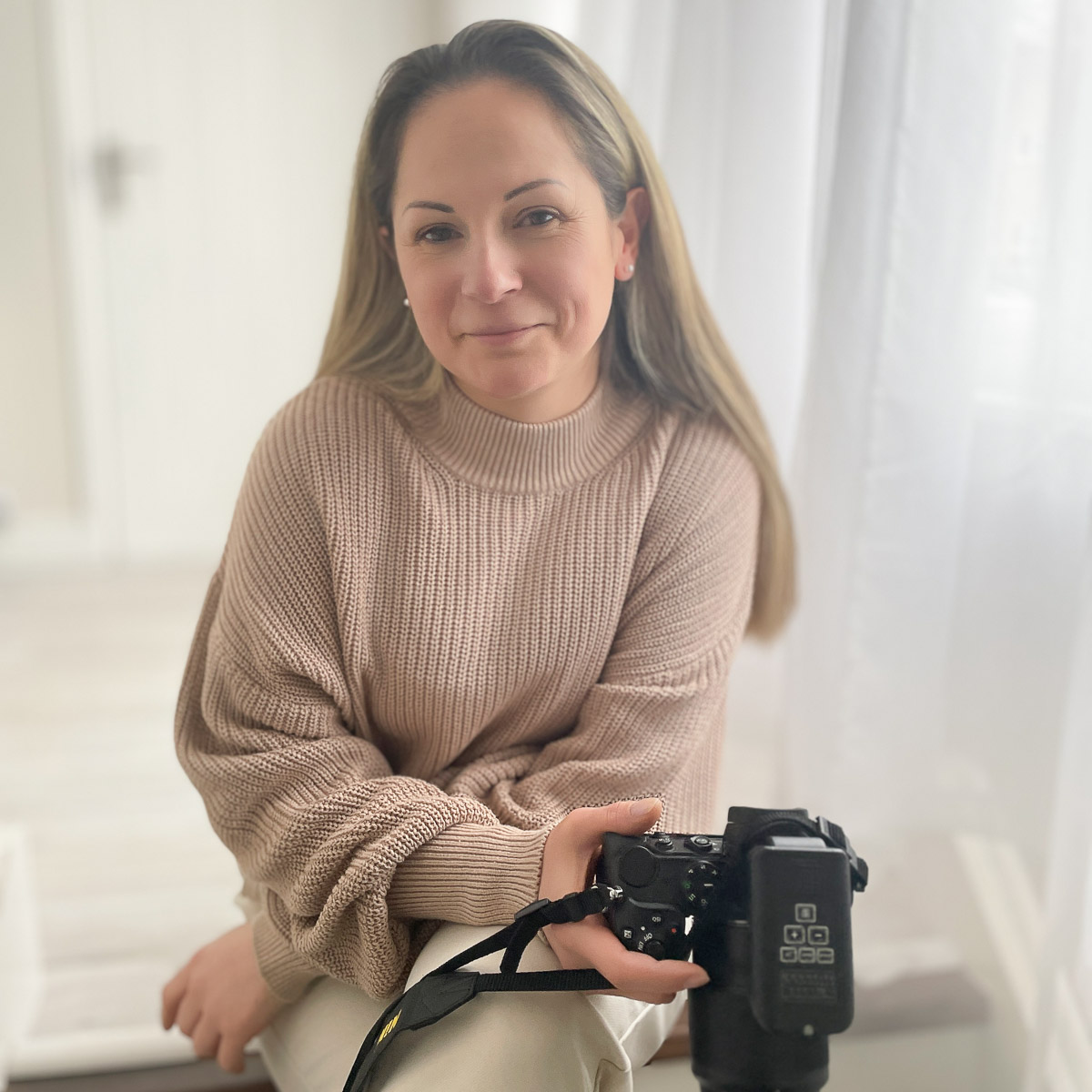 family photographer sitting on some wooden steps holding a professional camera and smiling