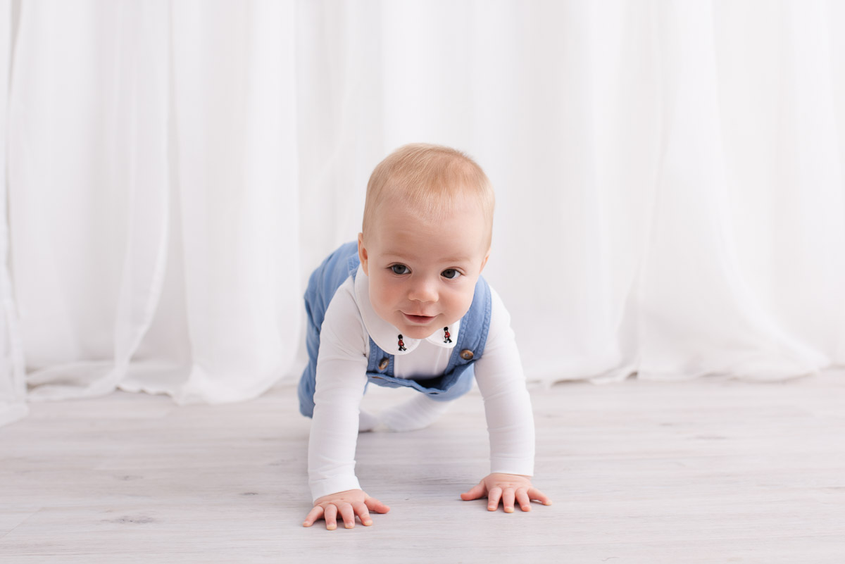 Boy in blue Trotter dungarees starting to crawl towards the child photographer in their Oxfordshire studio