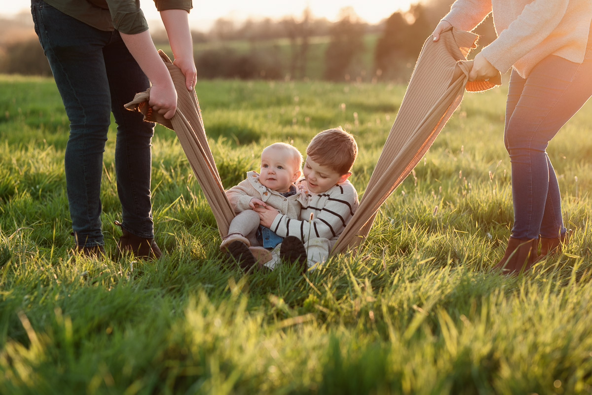 Siblings being swung by their parents with the sun setting behind