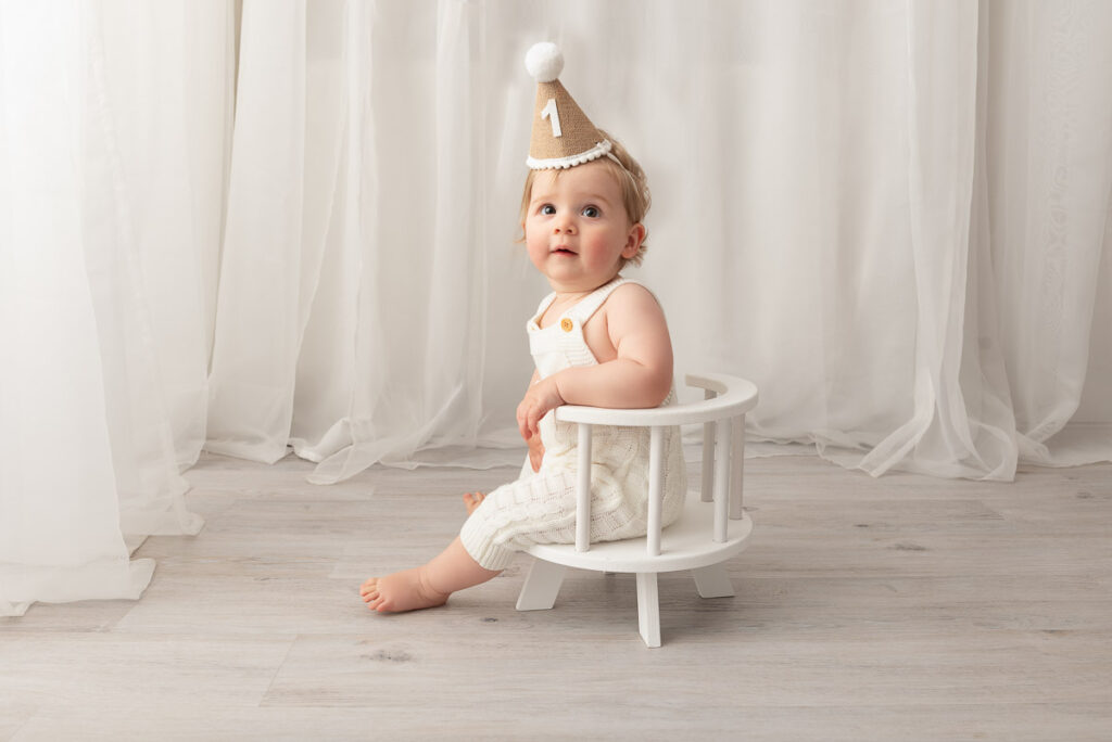 Birthday boy sits on a mini wooden chair wearing his party hat