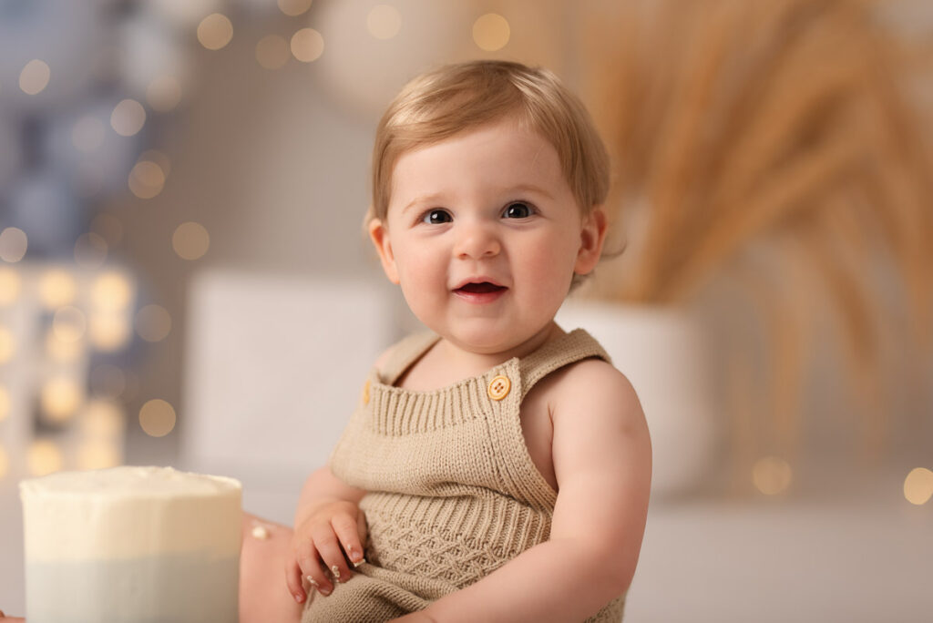 Close up of boy sitting next to his first birthday cake