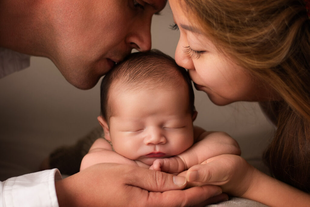 A family photographer in Oxfordshire captures an image of mum and dad kissing their newborn baby on the head