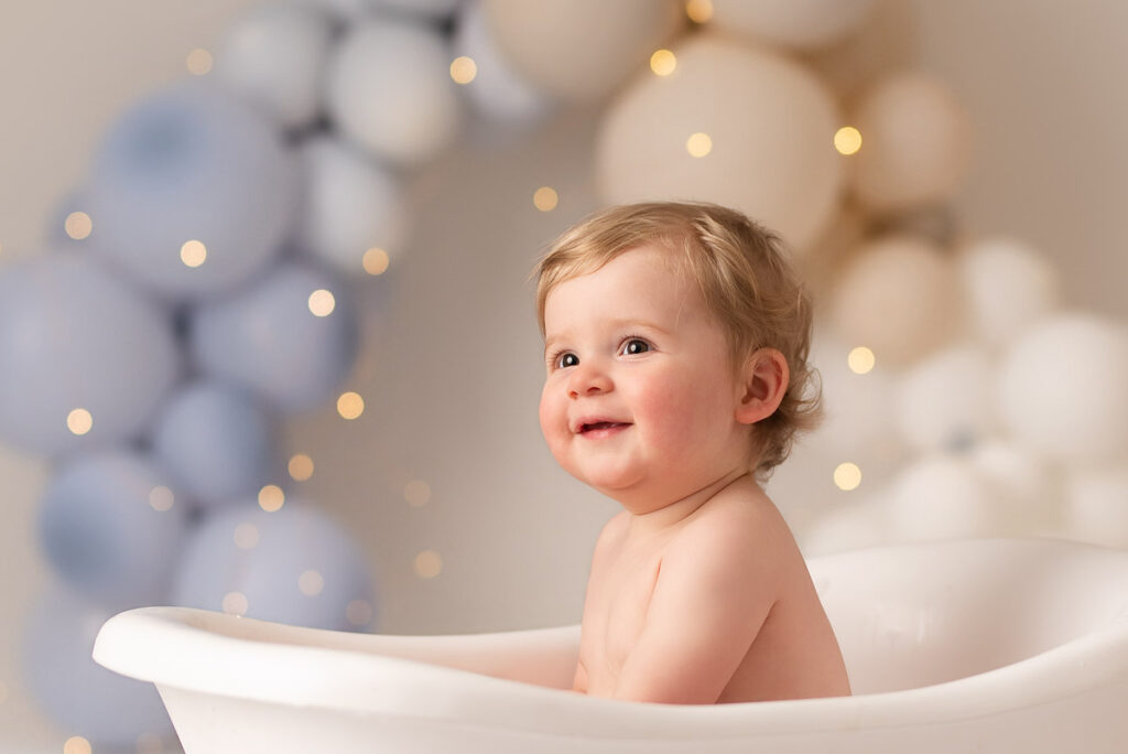 Smiling boy sits in a mini bath tub for this cake smash photographer in Oxfordshire