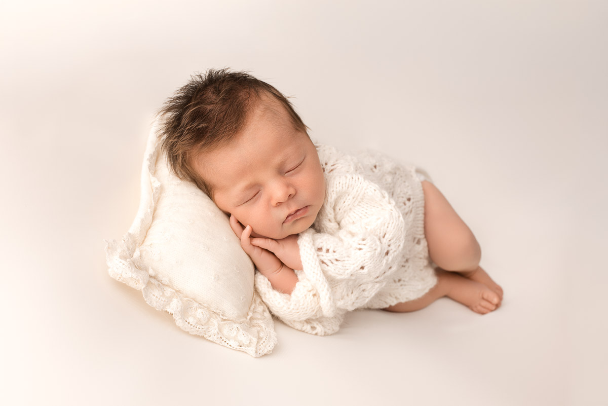 Newborn baby girl sleeps on her side having been posed by the photographer