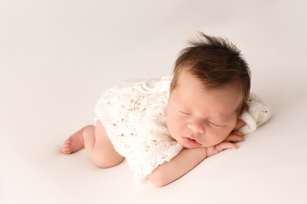 Baby girl lies on her front wearing white knitted romper