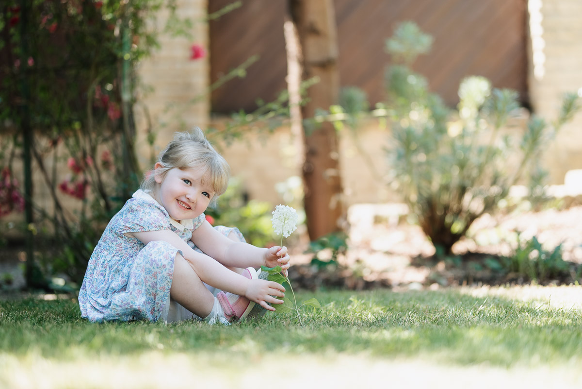 Little girl sits on the grass in her garden holding a white flower