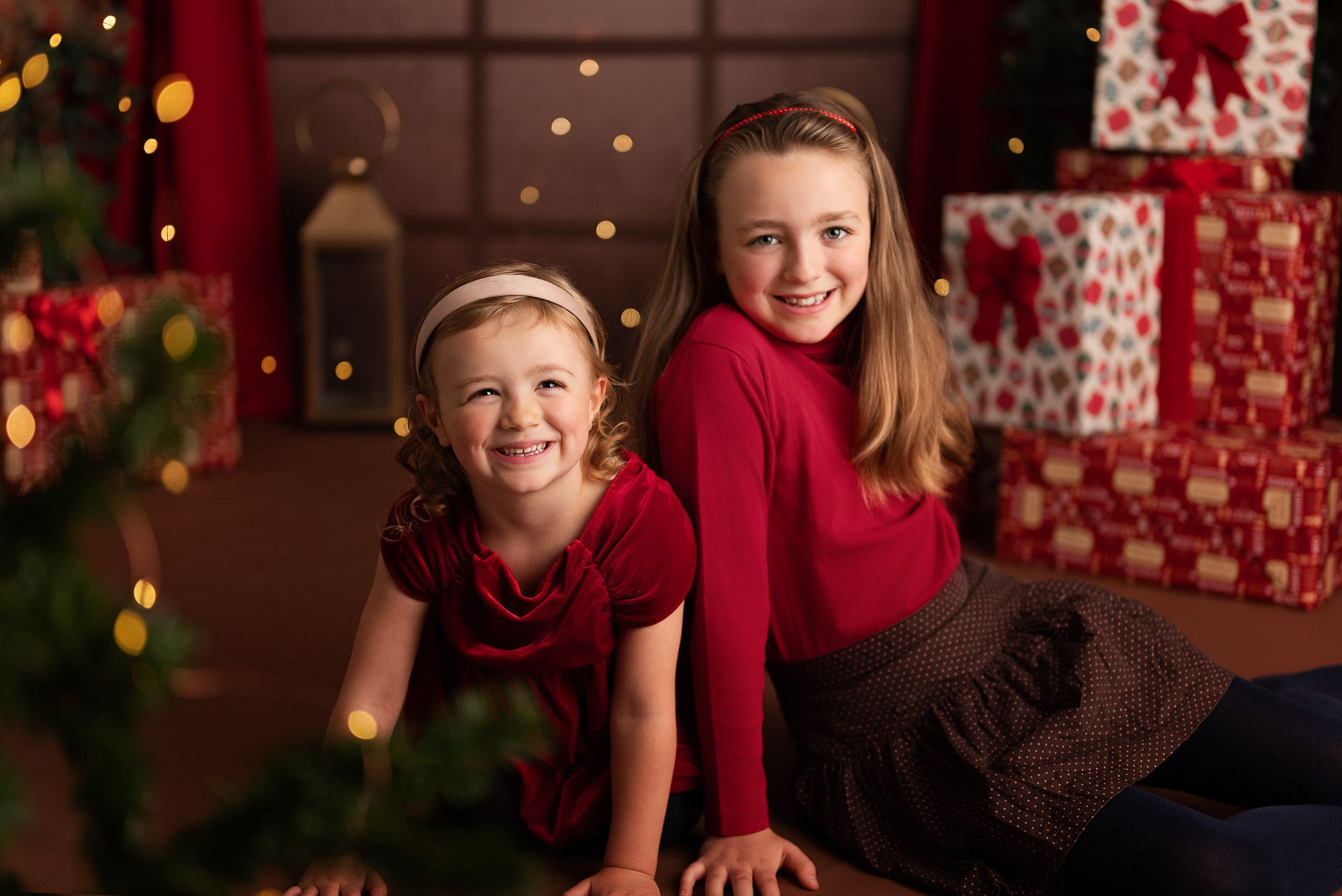 Two girls sit surrounded by red and gold presents during their annual Christmas family photoshoot