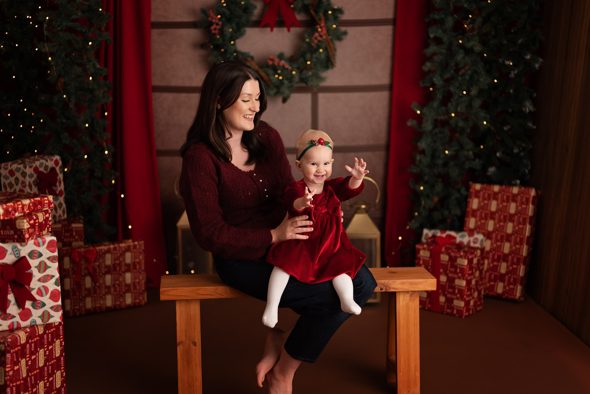 Mother an daughter sit on a wooden bench surrounded by Christmas presents and twinkly lights