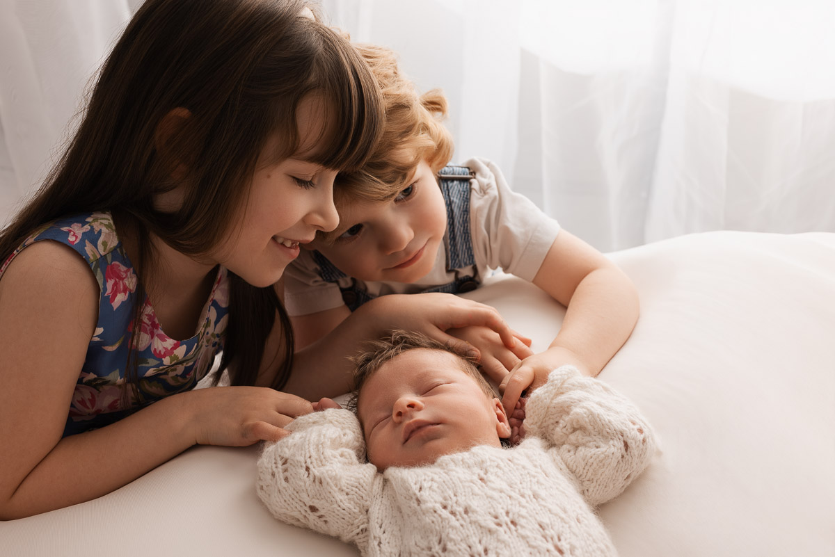 Baby's brother and sister hold her hands during the family baby photoshoot