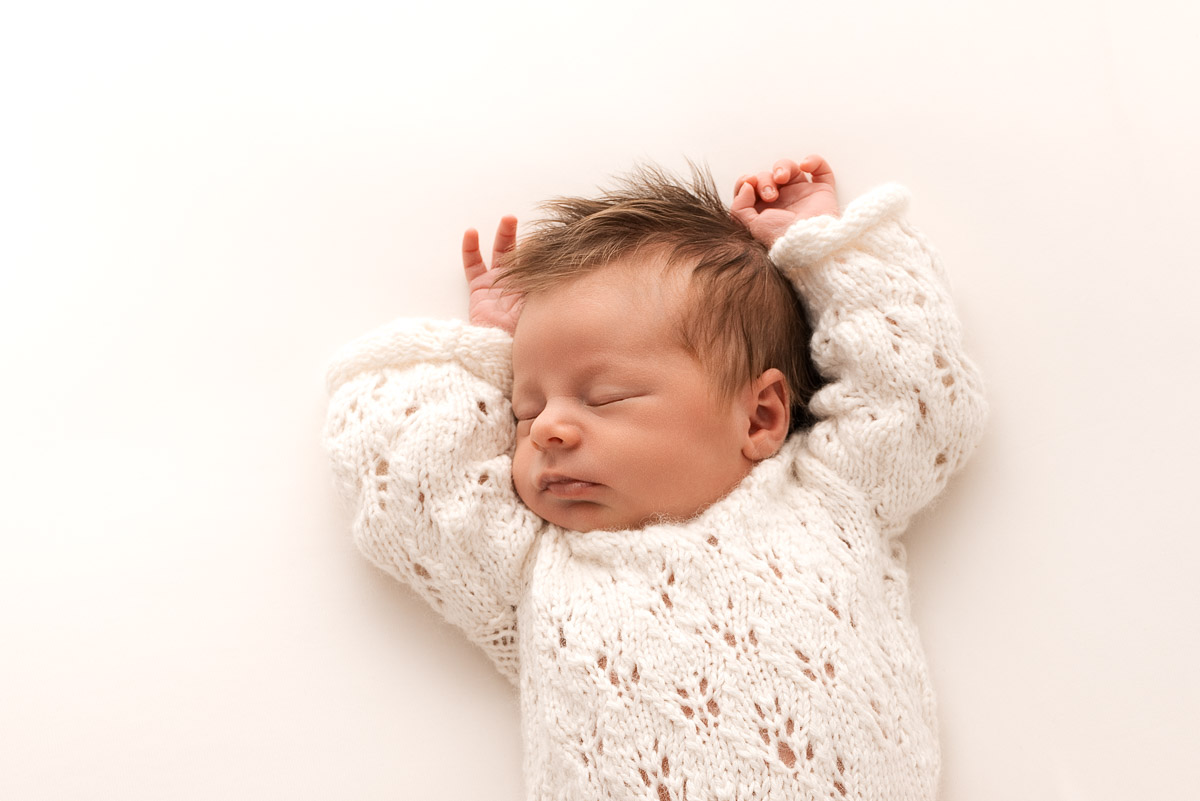 Baby girl is photographed fast asleep from above with her hands over her head