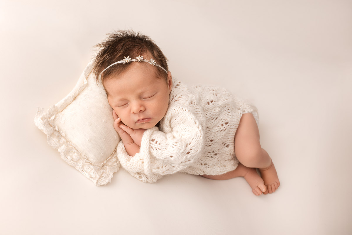 Baby girl wearing knitted white outfit and a delicate headband with three silver stars in it