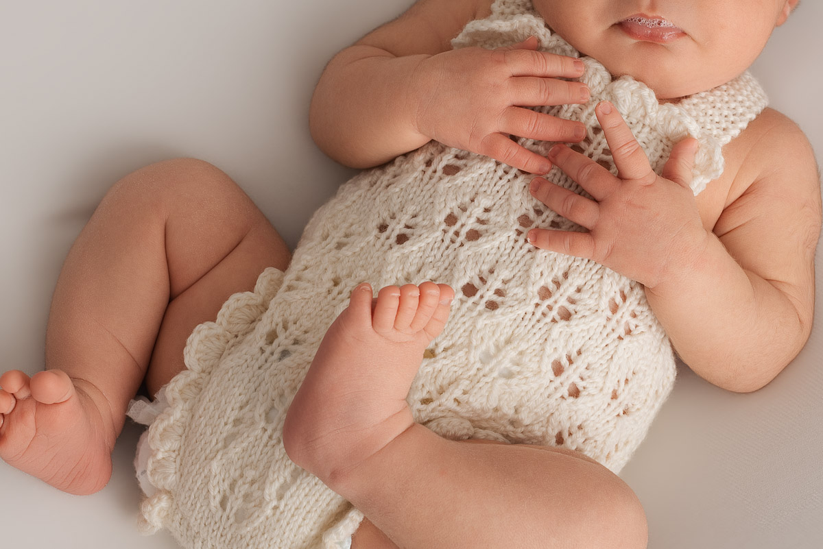 Baby girl wearing cream romper lies on her back.