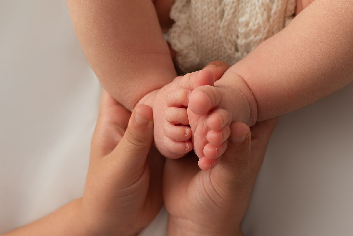 A close up photo of big sisters hands holding newborn babys feet