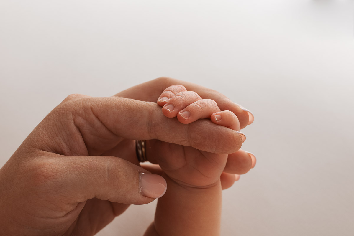 A baby's arm in held in the air with her fingers clinging on to her mothers finger