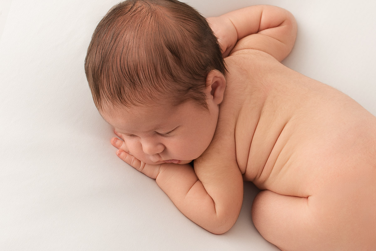 Baby girl is asleep on her front. The photographer has posed her to show off her fat rolls