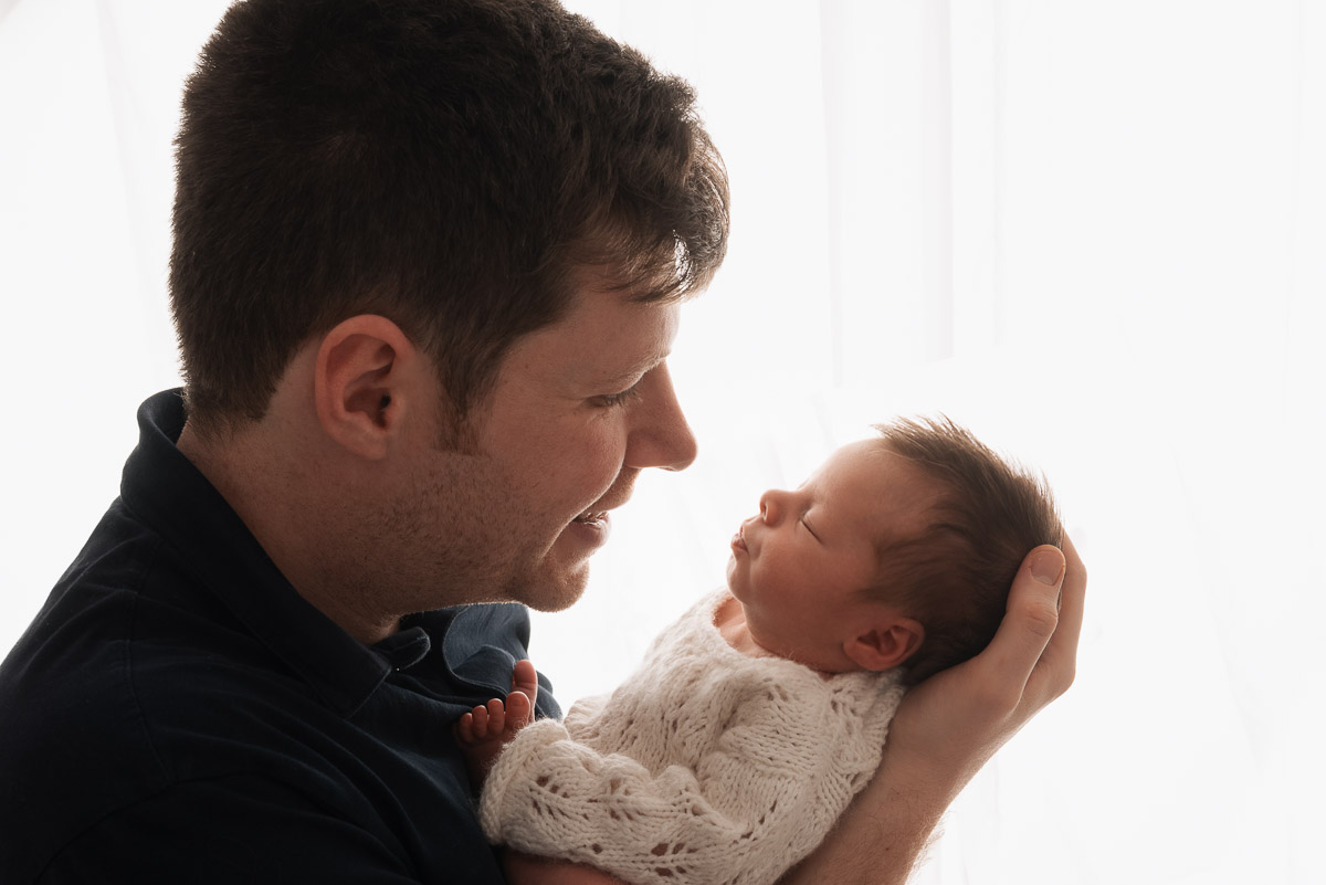 Father holds his newborn baby in his arms and looks at her adoringly