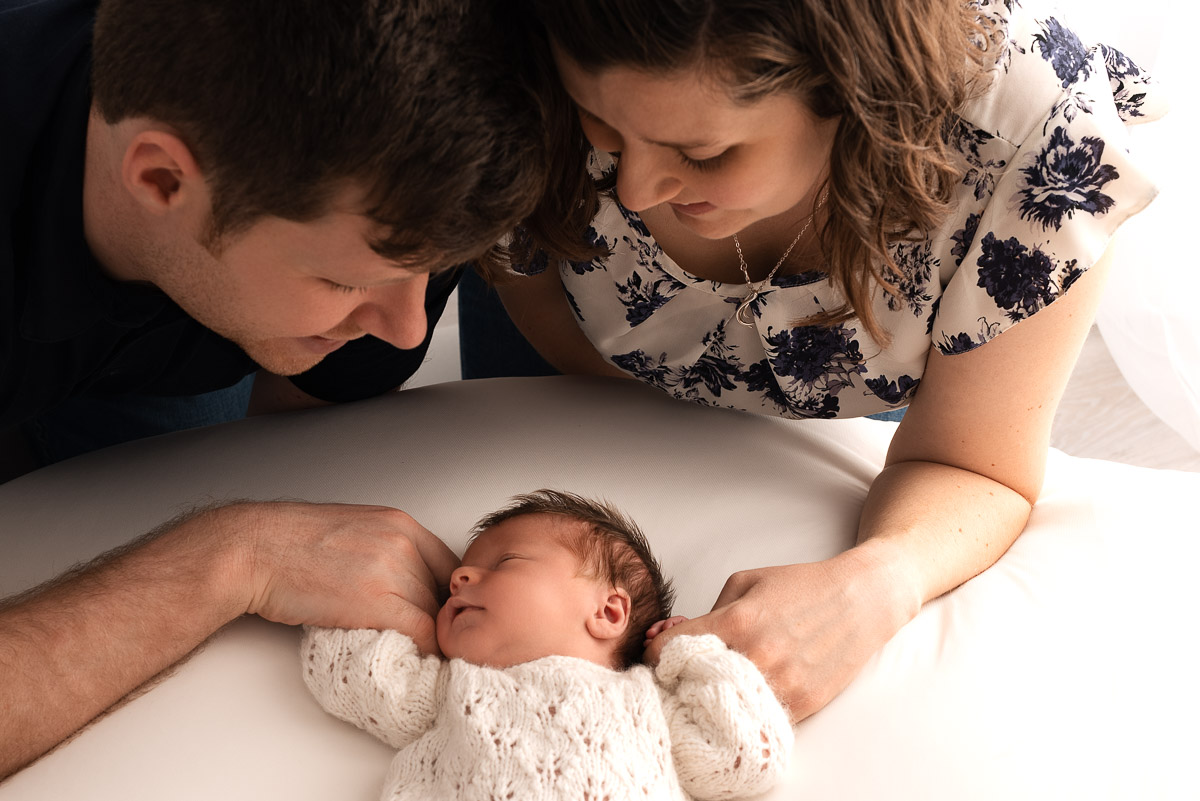 Mummy and daddy lean over their newborn baby who is lying on the photographers beanbag