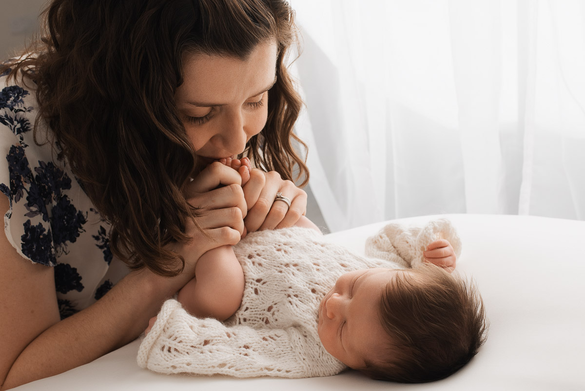 Mother kissing her newborn daughters feet during her baby photoshoot